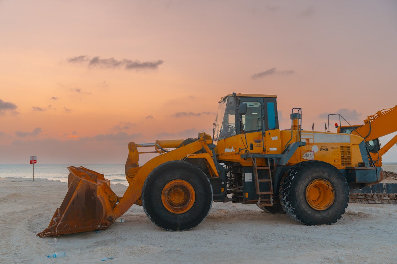 A bulldozer at a beach construction site during sunset, ready for the next days work.  Yellow bulldozer at a beach construction site during sunset with a beautiful orange sky.